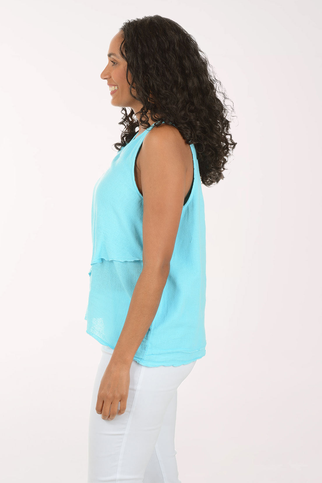 Woman wearing a light blue sleeveless top and white pants on a white background