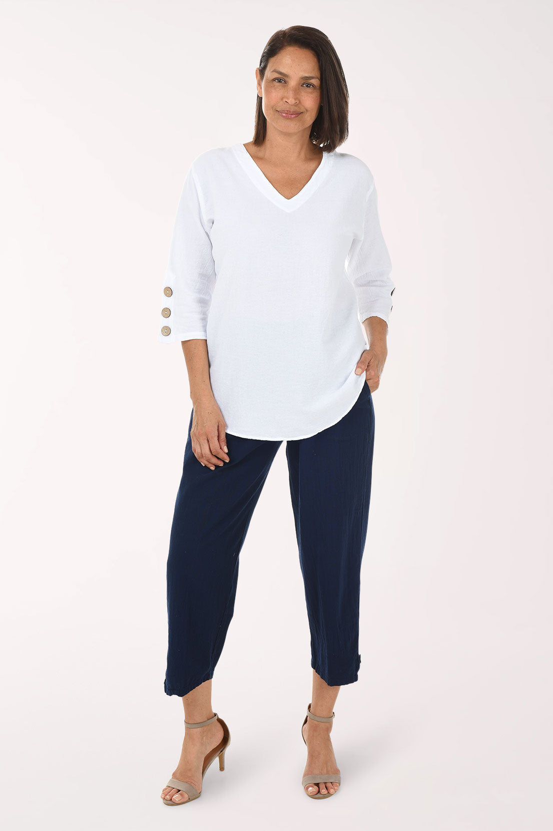 Woman wearing a white blouse with button details and navy pants on a white background
