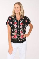 Woman wearing a black floral blouse with pink roses on a white background