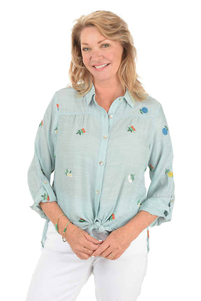 Woman wearing a light blue shirt with floral embroidery on a white background.