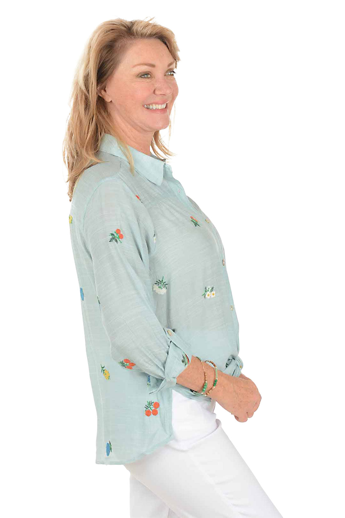 Woman wearing a light blue shirt with floral embroidery on a white background. Side shot.