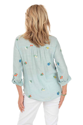Woman wearing a light blue shirt with floral embroidery on a white background. Back shot.