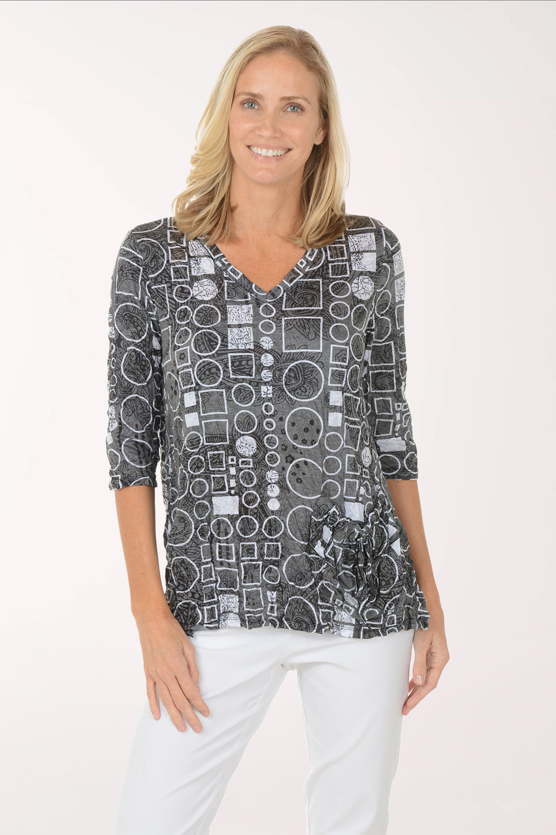 Woman wearing a patterned top and white pants on a white background