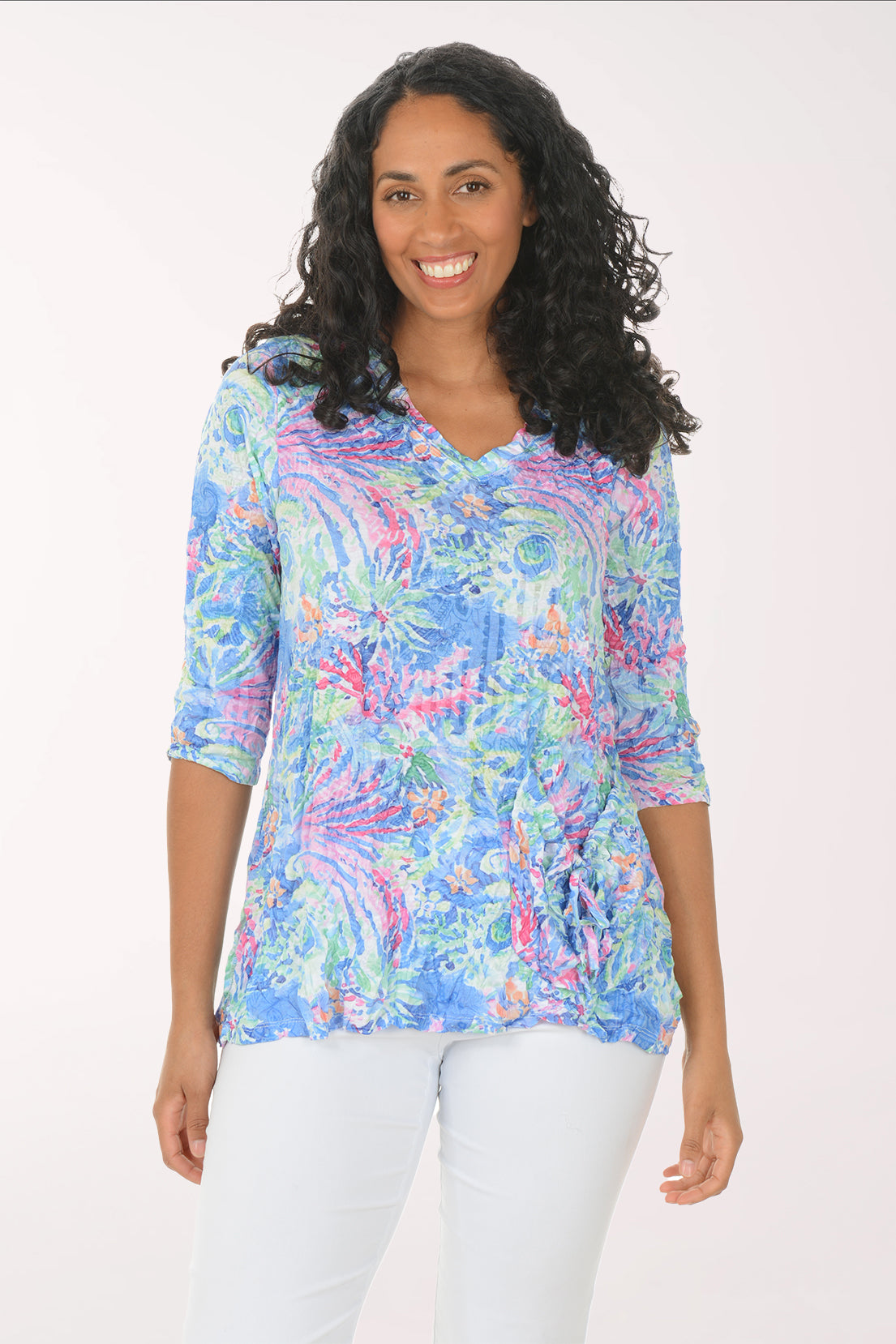 Woman wearing a colorful patterned blouse with white pants on a white background