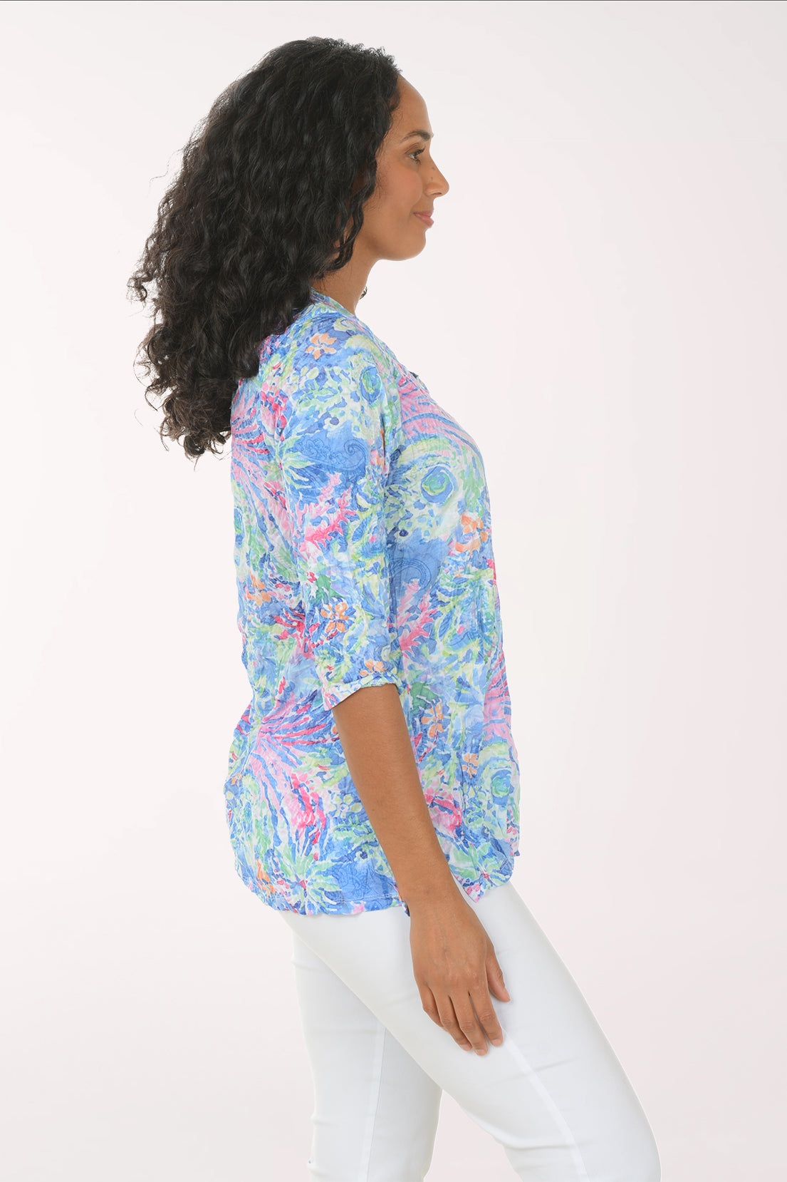 Woman wearing a colorful patterned blouse with white pants on a white background