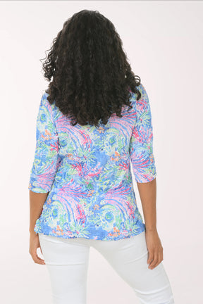 Woman wearing a colorful patterned blouse with white pants on a white background