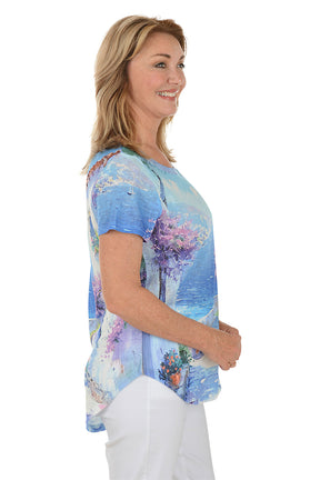 Woman wearing a colorful beach-themed t-shirt with a scenic design. Side shot.