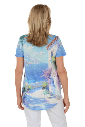 Woman wearing a colorful beach-themed t-shirt with a scenic design. Back shot.
