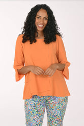 Woman wearing an orange top and colorful pants on a white background