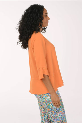 Woman wearing an orange top and colorful pants on a white background. Side shot