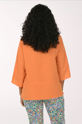 Woman wearing an orange top and colorful pants on a white background. Back shot.