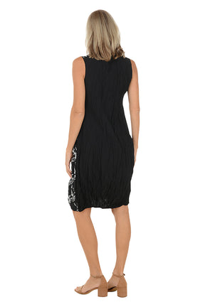 Woman wearing a black and white sleeveless dress with a left hip pocket.  Back shot.