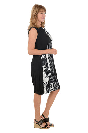 Woman wearing a black and white sleeveless dress with a pocket on the left side and an asymmetrical hem. Side shot.