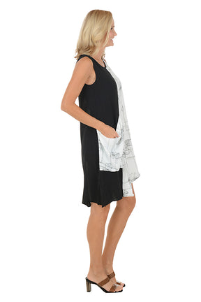 Woman wearing a black and white sleeveless dress with a large pocket on the left side and an asymmetrical hem. Side shot.