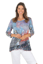 Woman wearing a colorful patterned top and white pants on a white background.