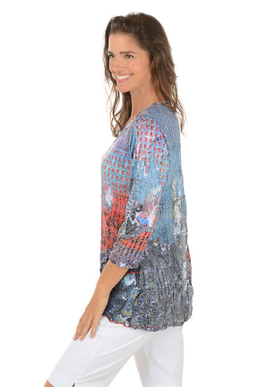 Woman wearing a colorful patterned top and white pants on a white background. Side shot.