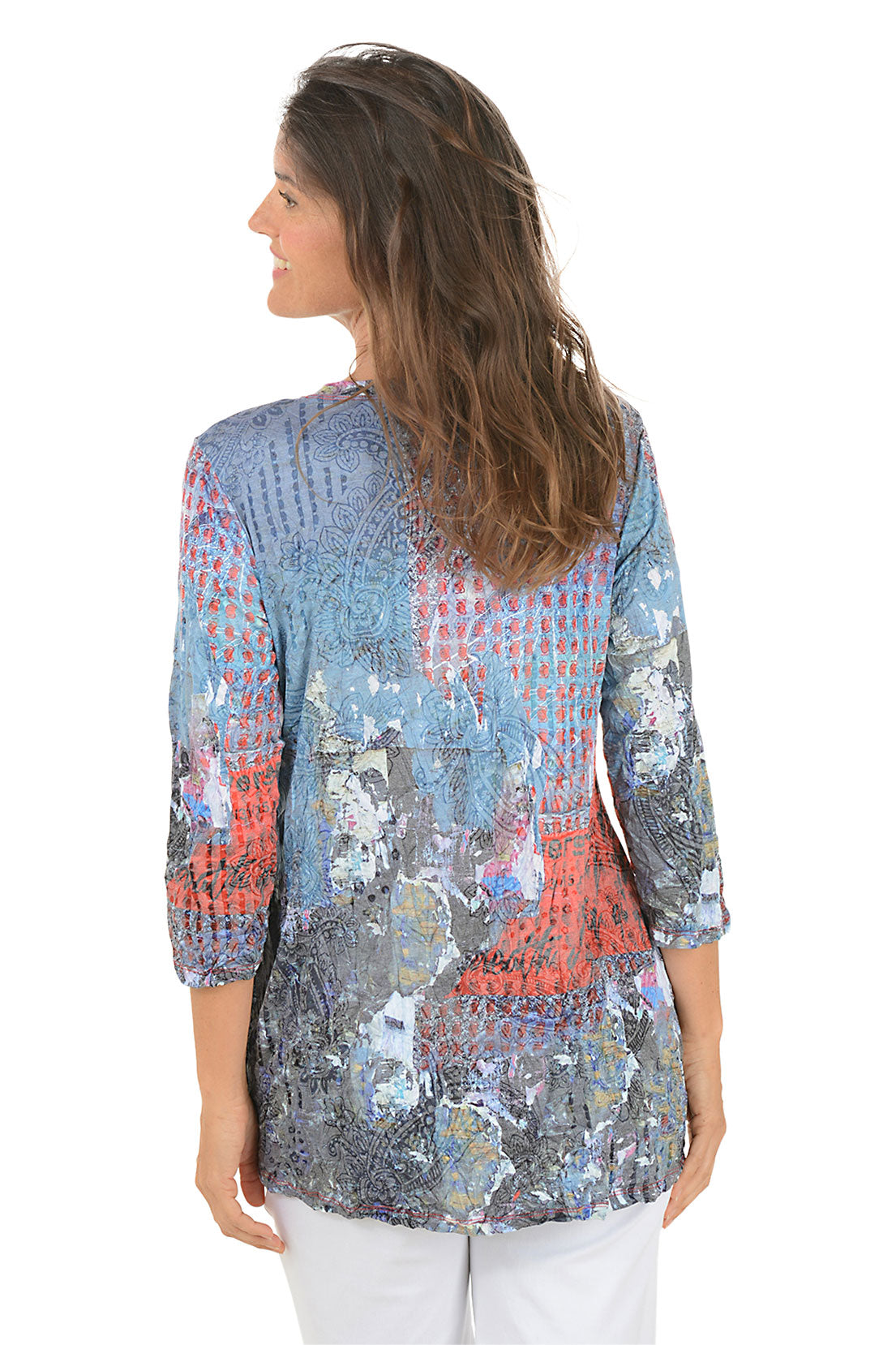Woman wearing a colorful patterned top and white pants on a white background. Back shot.