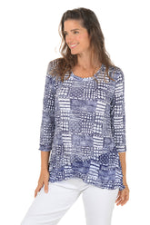 Woman wearing a blue patterned top and white pants on a white background.