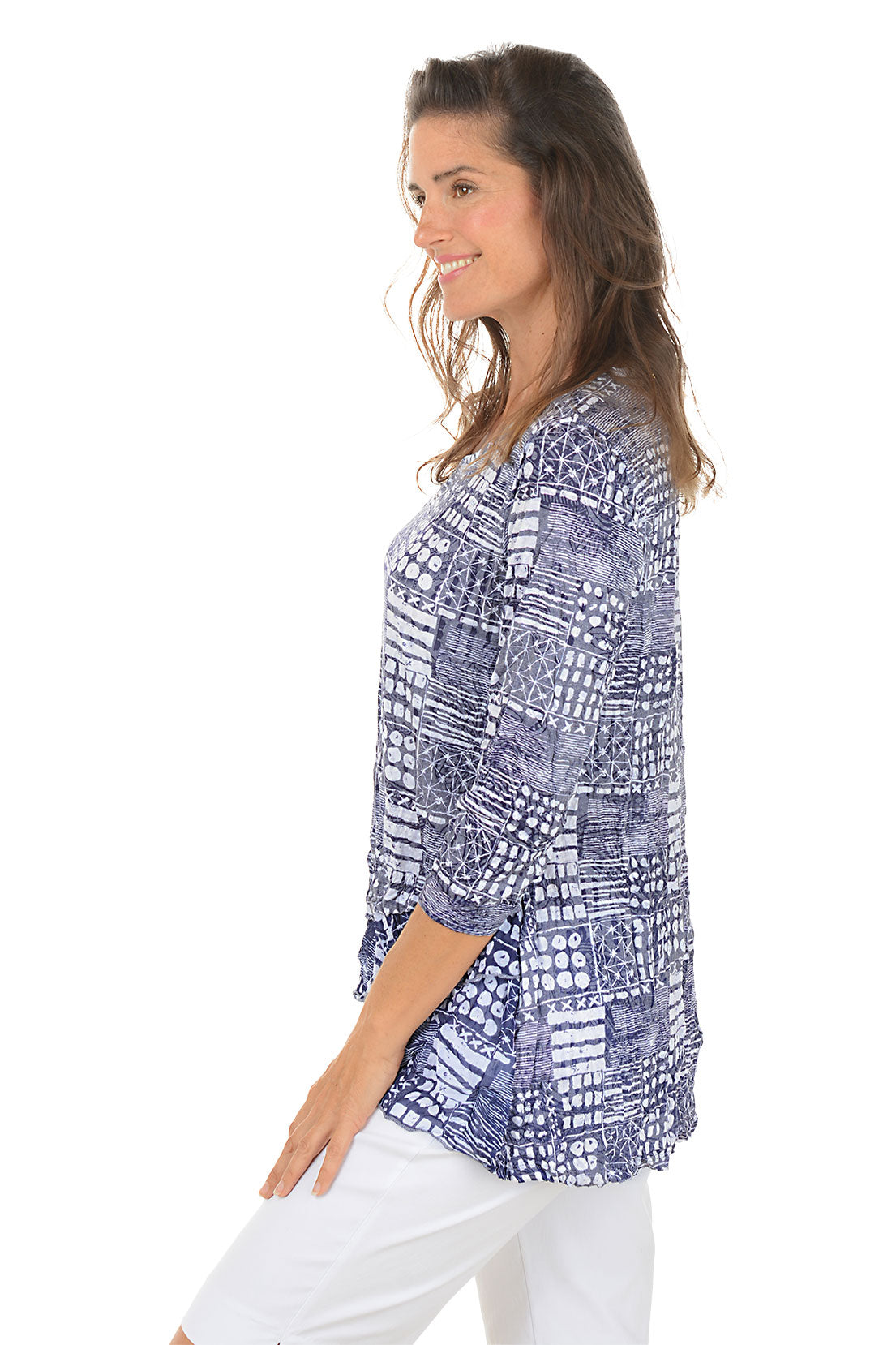 Woman wearing a blue patterned top and white pants on a white background. Side shot.
