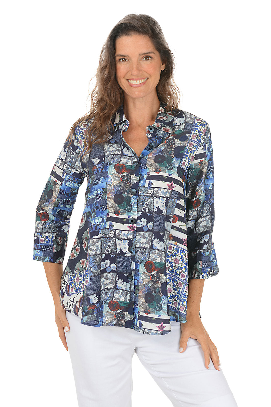 Woman wearing a colorful patchwork navy blouse with white pants on a white background.