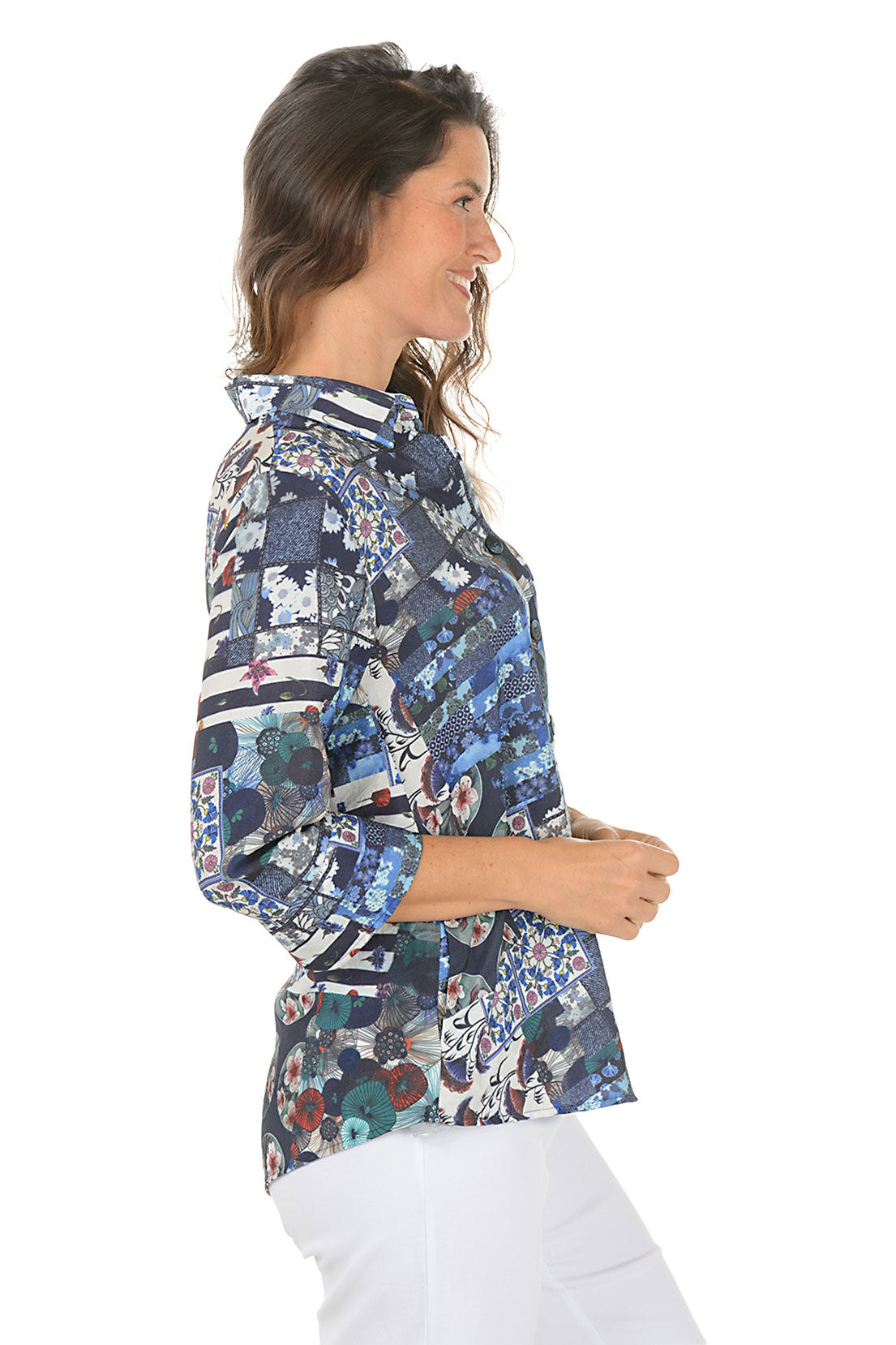 Woman wearing a colorful patchwork navy blouse with white pants on a white background. Side shot.