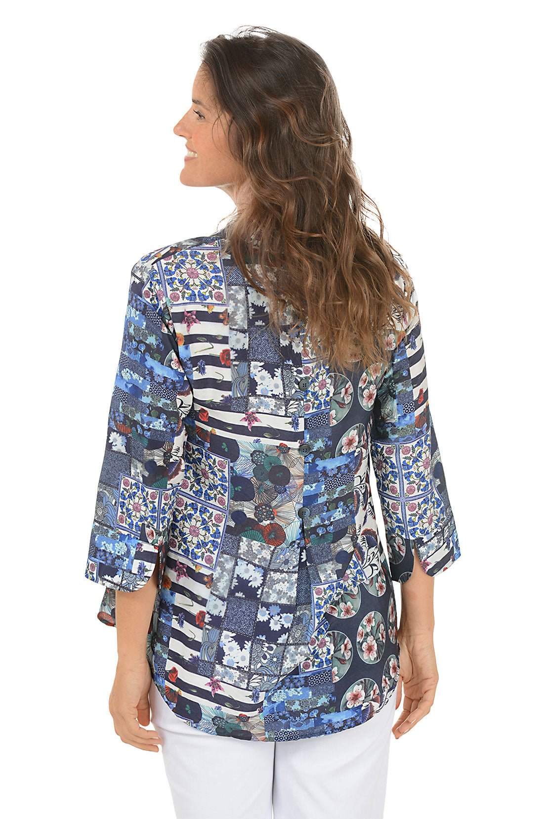 Woman wearing a colorful patchwork navy blouse with white pants on a white background. Back shot.
