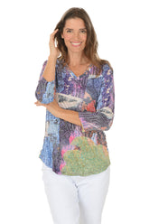 Woman wearing a 3/4 sleeve colorful hemline patterned blouse with a white background.