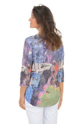 Woman wearing a 3/4 sleeve colorful hemline patterned blouse with a white background. Back shot.