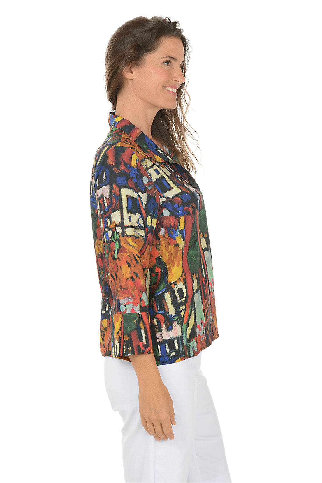 Woman wearing a colorful patterned blouse with white pants on a white background. Side shot.