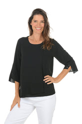 Woman wearing a black blouse with sheer sleeves on a white background.