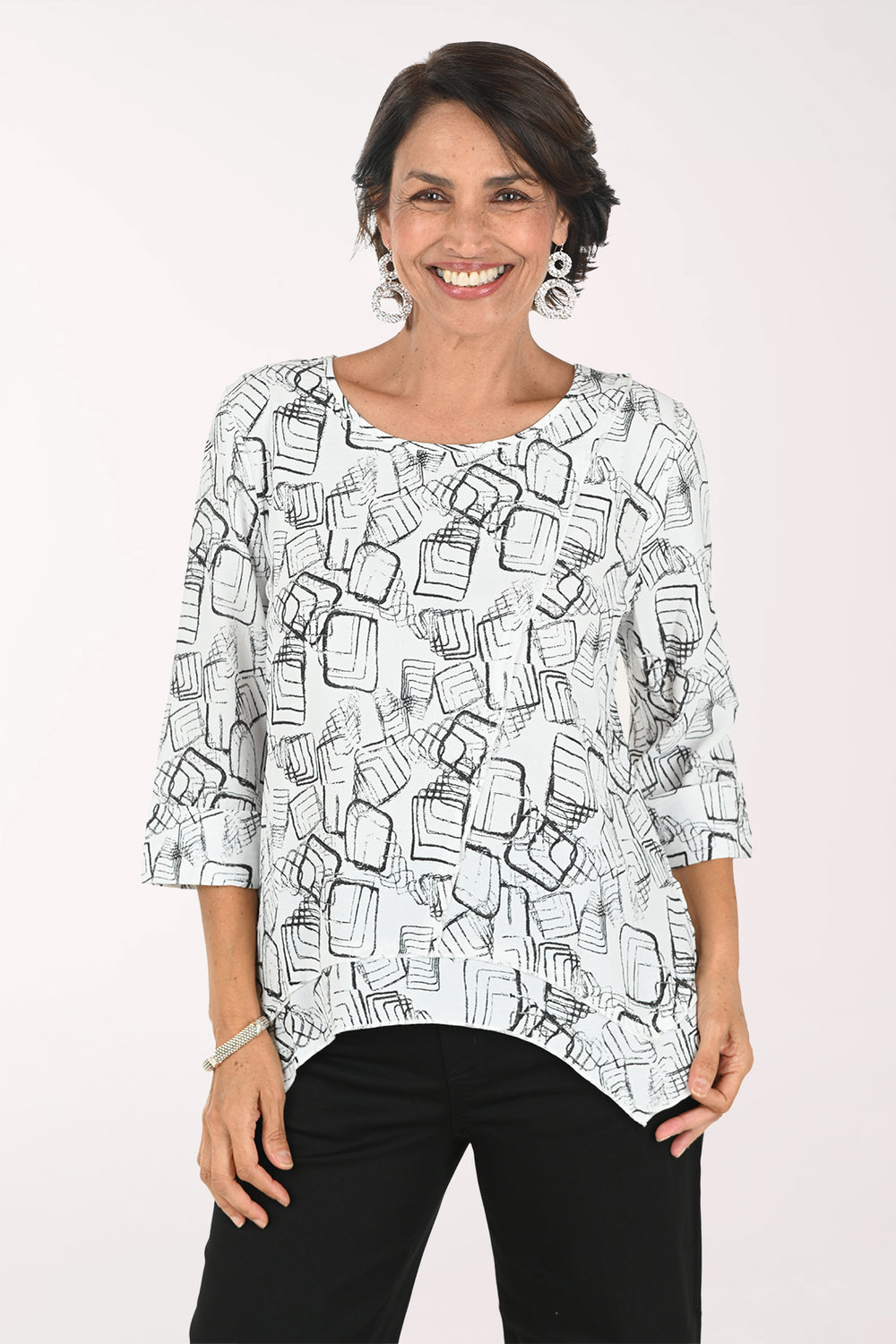 A woman modeling a white three-quarter sleeve top with a black abstract line print, paired with black pants, against a plain white background.