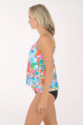 Woman wearing a colorful floral tank top and black shorts on a white background. Side shot.