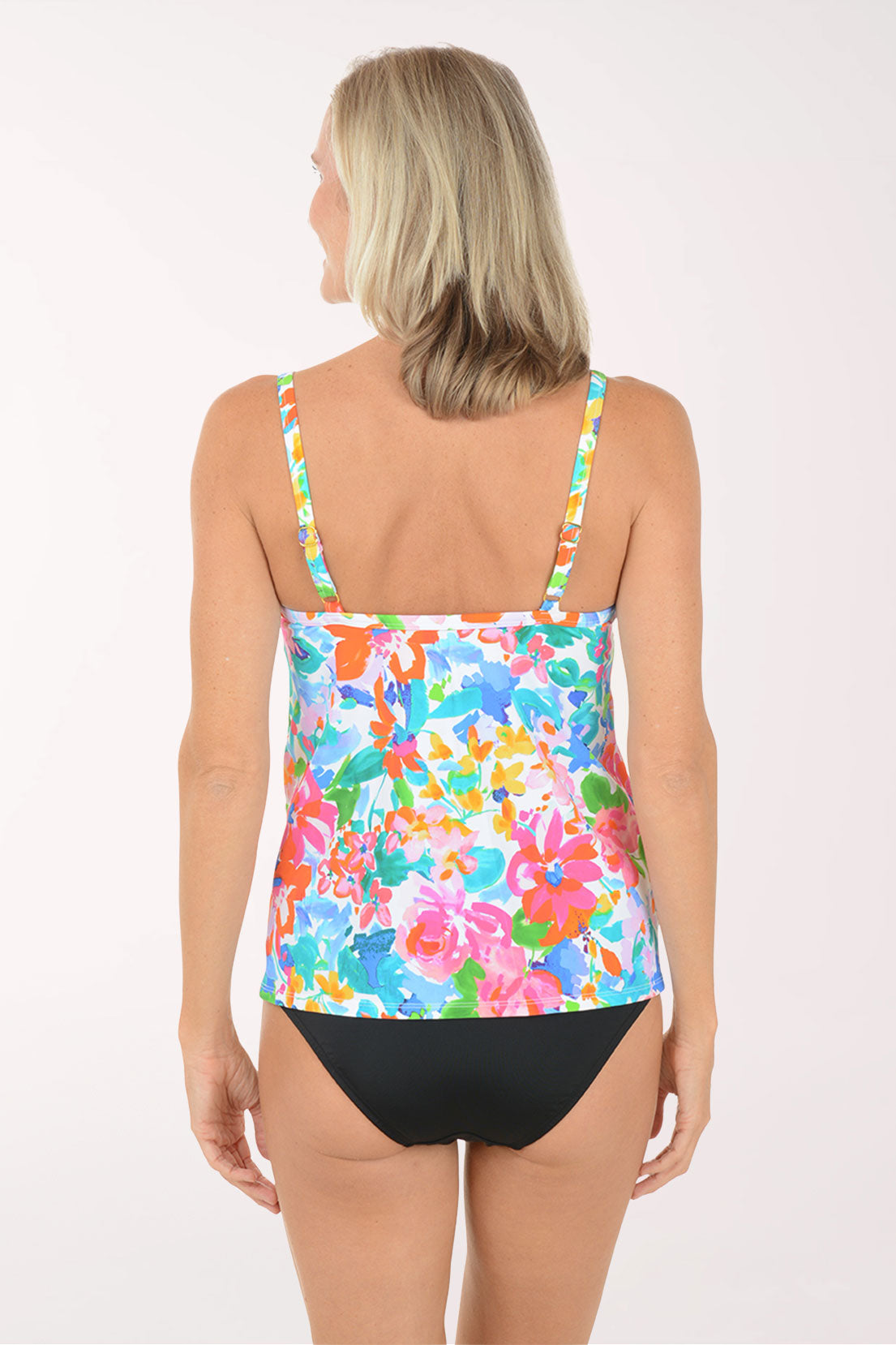 Woman wearing a colorful floral tank top and black shorts on a white background.  Back shot.