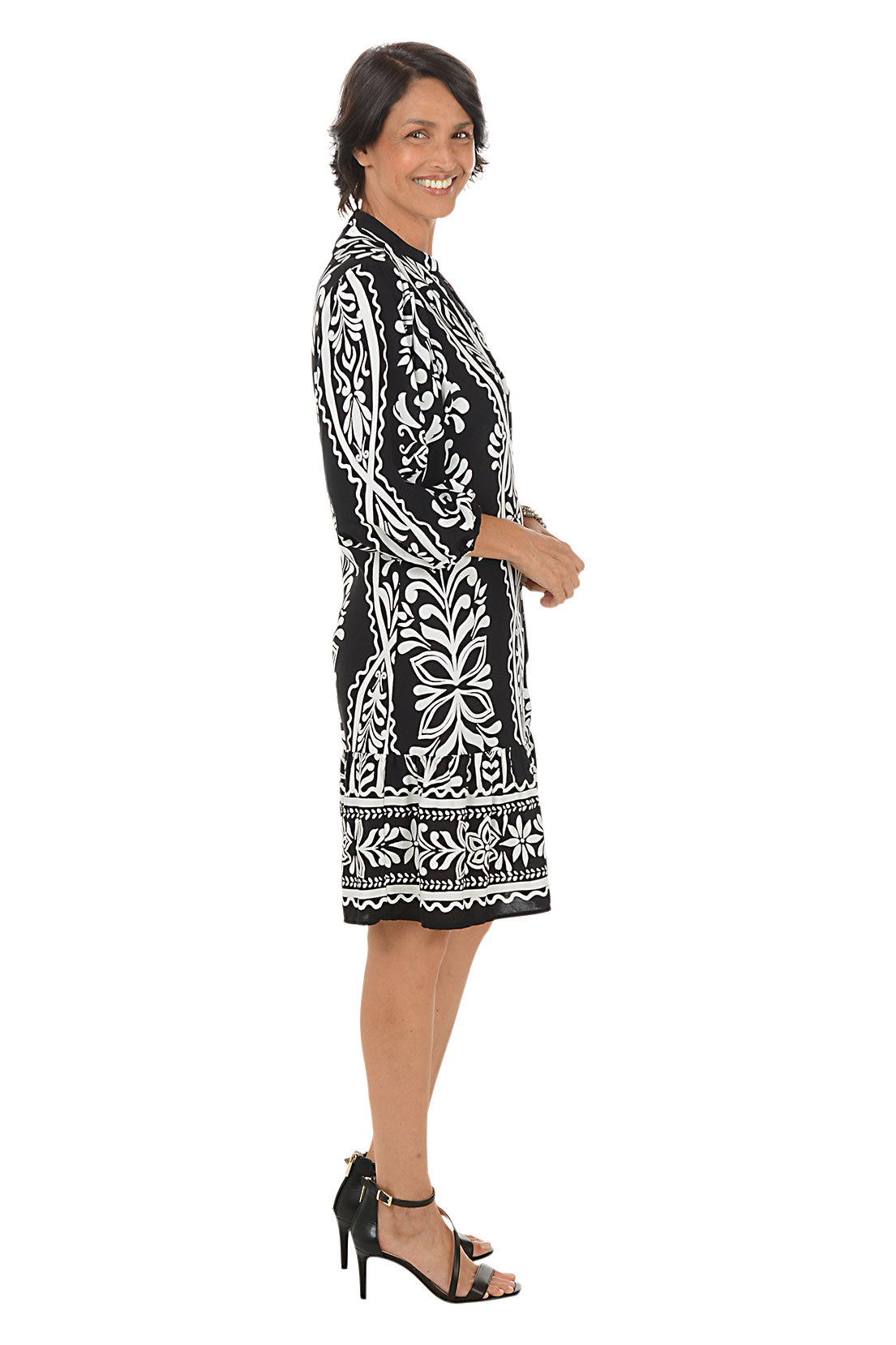 Woman wearing a black and white patterned dress on a white background. Side shot.