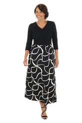 Woman wearing a 3/4 sleeve black and white patterned maxi dress on a white background. Side shot.