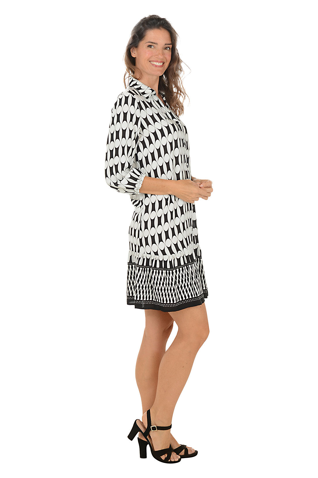 Woman wearing a 3/4 sleeved black and white patterned dress on a white background. Side shot.