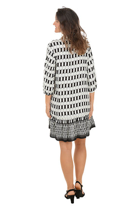 Woman wearing a 3/4 sleeved black and white patterned dress on a white background. Back shot.