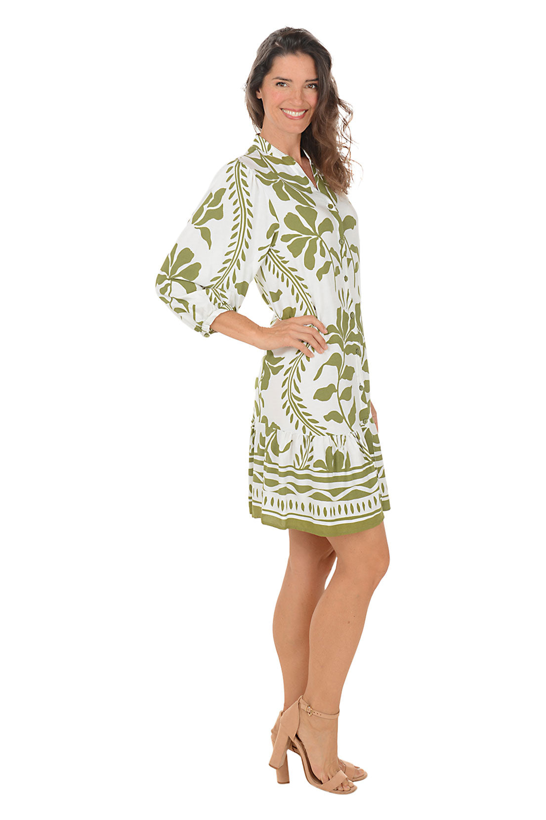 Woman wearing a 3/4 sleeved green and white floral vine patterned dress on a white background. Side shot.