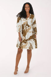 A woman modeling a short tiered dress with three-quarter sleeves, featuring an abstract botanical pattern in brown and beige on an off-white background, set against a plain white studio backdrop.