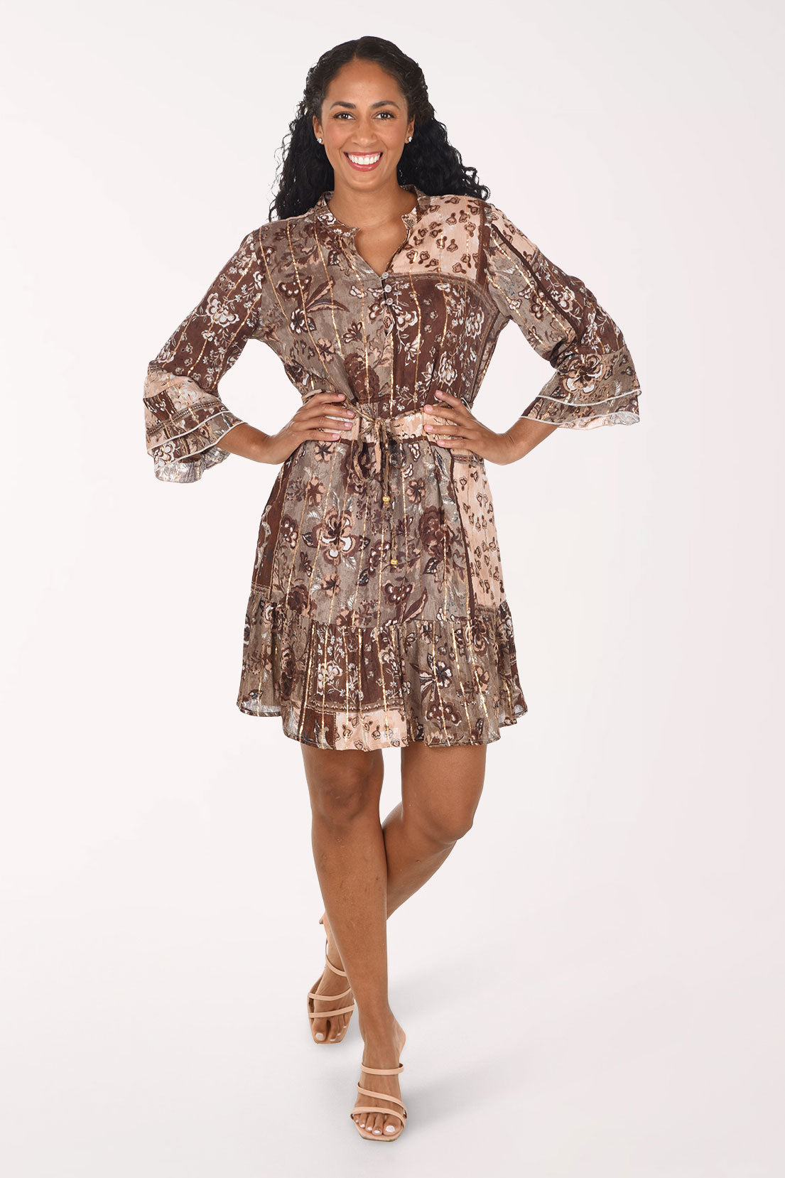 A woman modeling a brown and beige patterned mini dress with three-quarter bell sleeves and a tie waist, posed against a solid white studio background.
