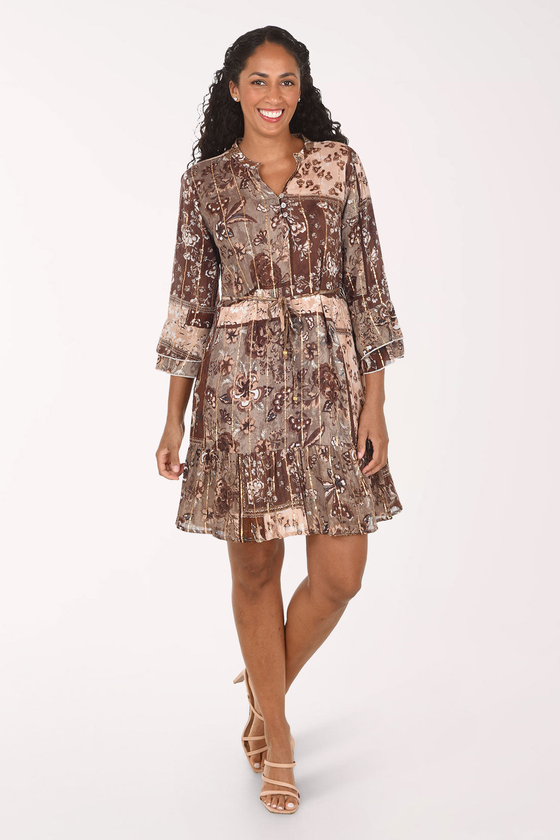 A woman modeling a brown and beige patterned mini dress with three-quarter bell sleeves and a tie waist, posed against a solid white studio background.