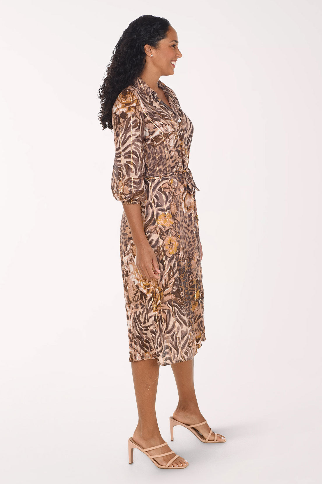 A woman modeling a knee-length button-up dress with a mixed animal print pattern in brown, beige, and black, paired with beige strappy high-heeled sandals against a plain white studio background.