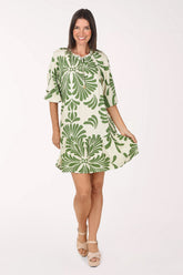 Model wearing the Mlle Gabrielle La Palma Drop Waist Dress, a cream dress with a bold green palm motif and elbow sleeves, front view