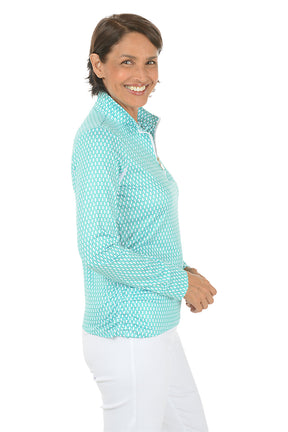 Woman wearing a light blue patterned shirt and white pants on a white background. Side shot.