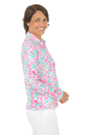 Woman wearing a colorful floral blouse with white pants on a white background. Side shot.