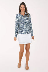 Woman wearing a floral long-sleeve top and white skirt on a light pink background