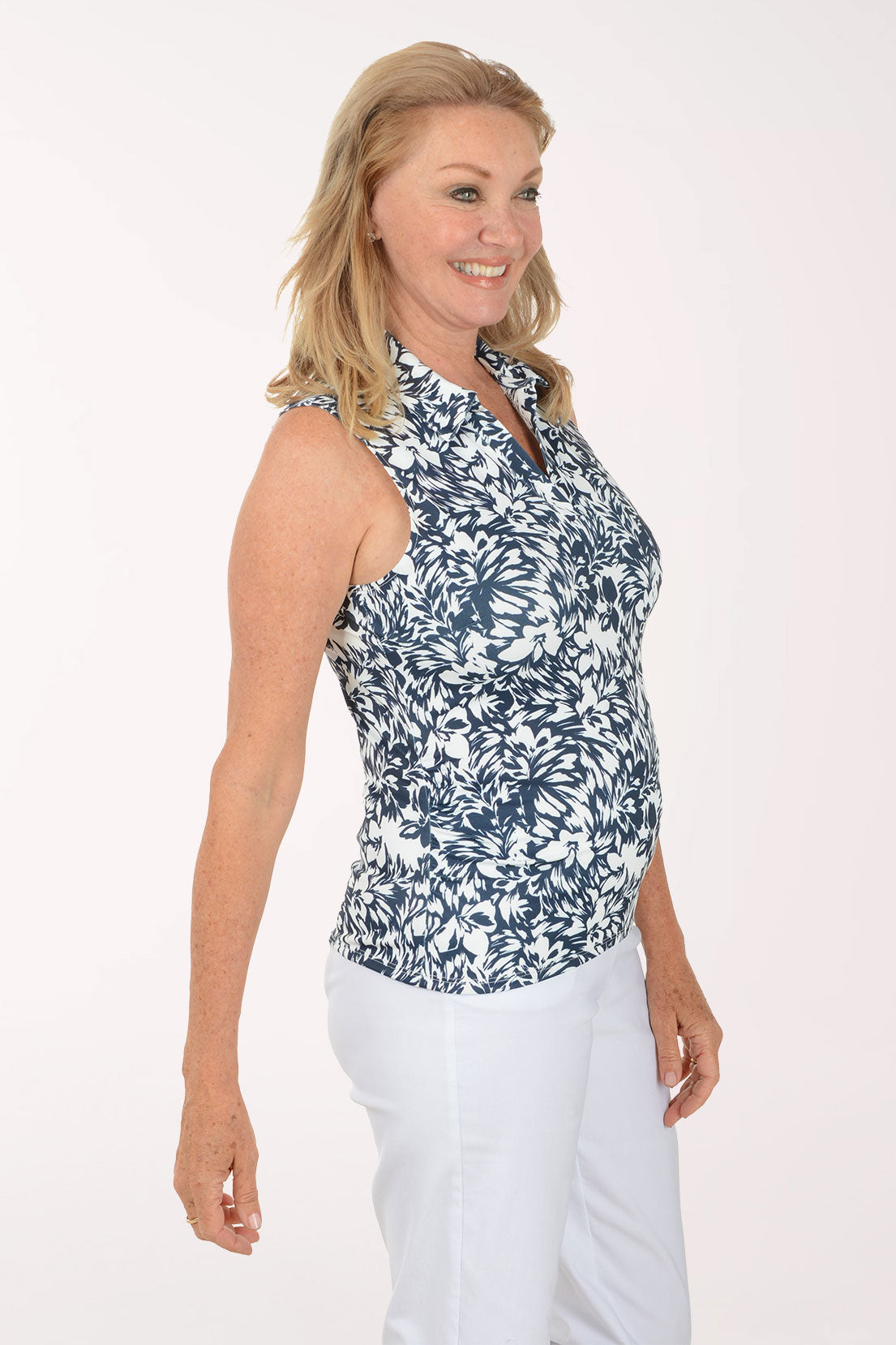 Woman wearing a sleeveless floral top and white pants on a plain background