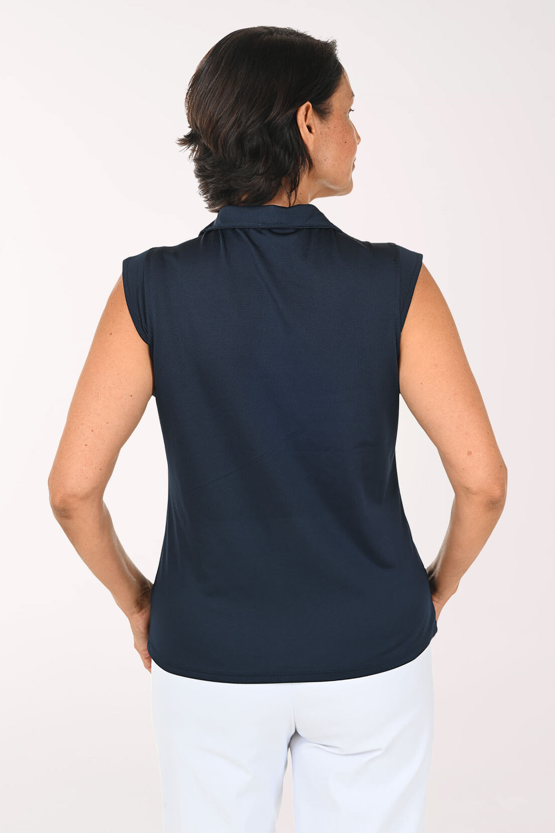 A woman shown from the back wearing a sleeveless navy blue collared top and white pants against a plain light background.
