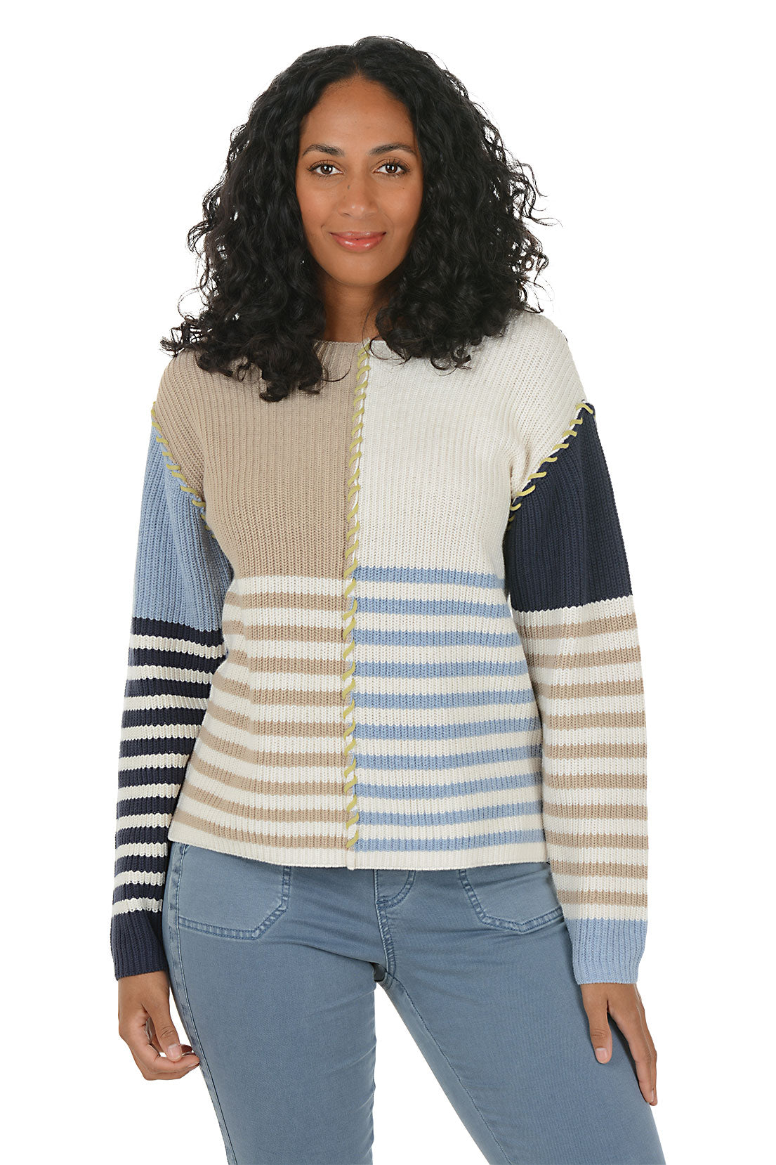 Woman wearing a colorful patchwork sweater boat neck sweater with blue jeans on a white background. Second front shot.