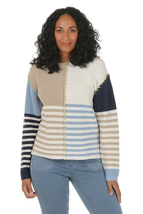 Woman wearing a colorful patchwork sweater boat neck sweater with blue jeans on a white background. Second front shot.